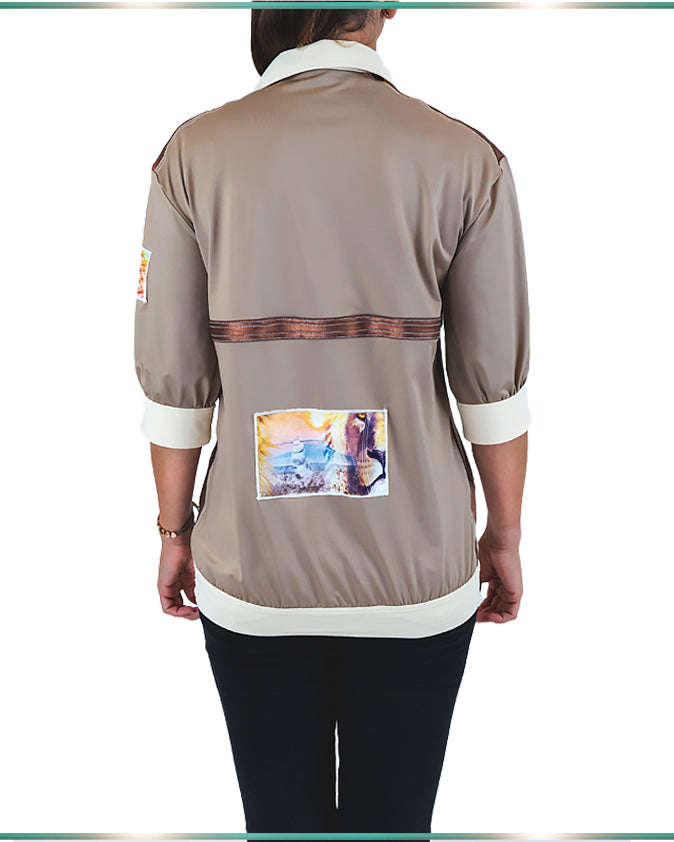 A model wearing a color-blocking blouse in neutral colors facing back showing the artwork on the back of the shirt.