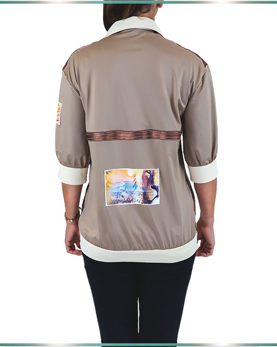 A model wearing a color-blocking blouse in neutral colors facing back showing the artwork on the back of the shirt.